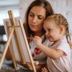 Mother teaching her daughter how to paint on canvas